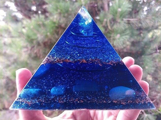 Blue Orgonite Pyramid with Quartz at the top in front of tree.